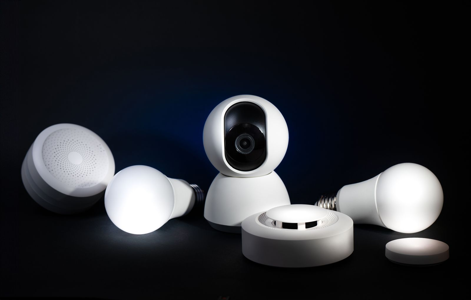 A home security camera, sensor, keypad and smart lock arranged on a dark studio backdrop.